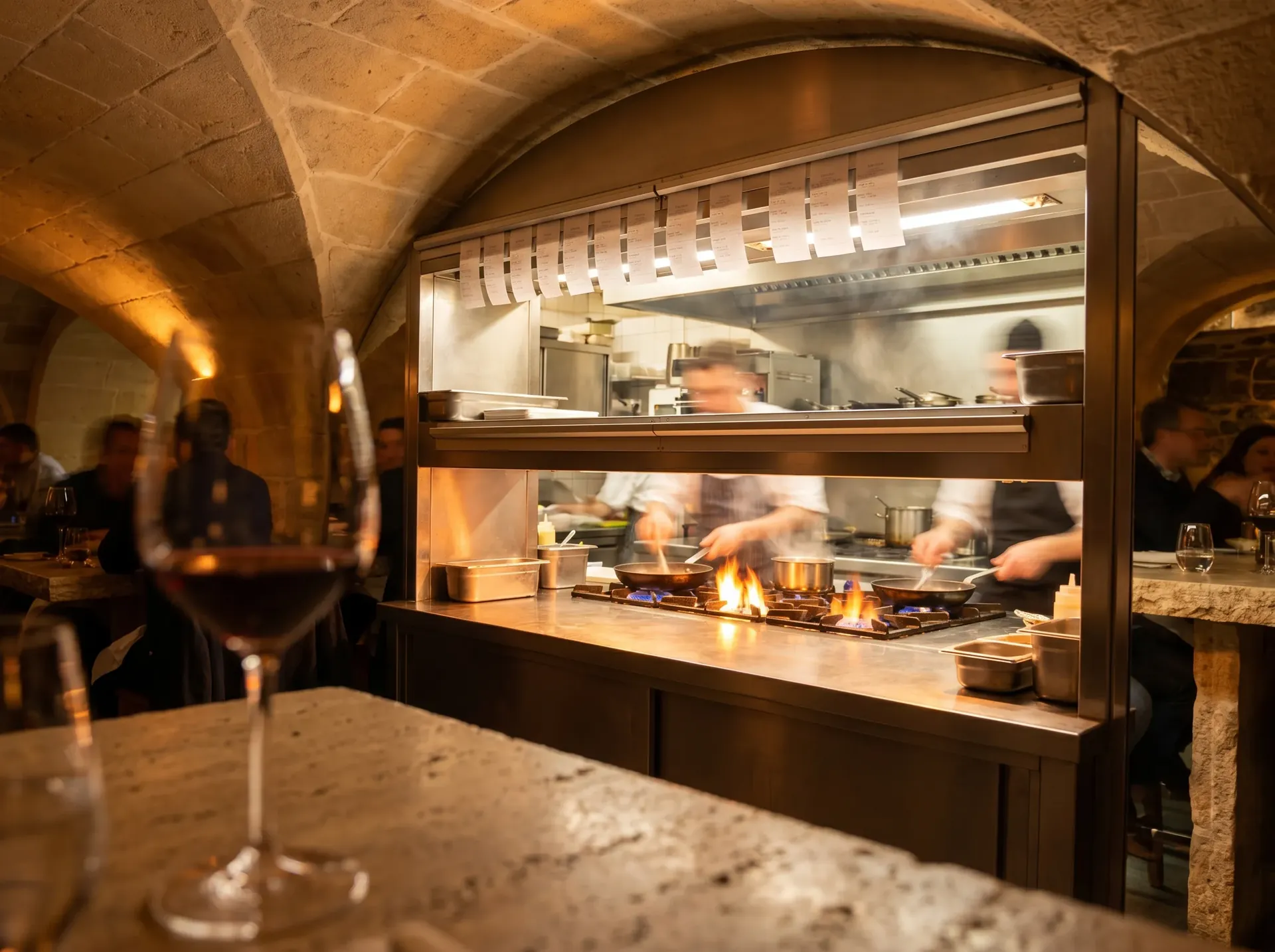 Vue depuis la table de fond — cuisine ouverte, service en cours